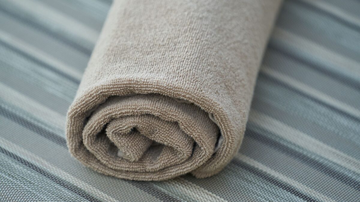 Une serviette de bain beige enroulée sur une surface rayée grise et blanche.