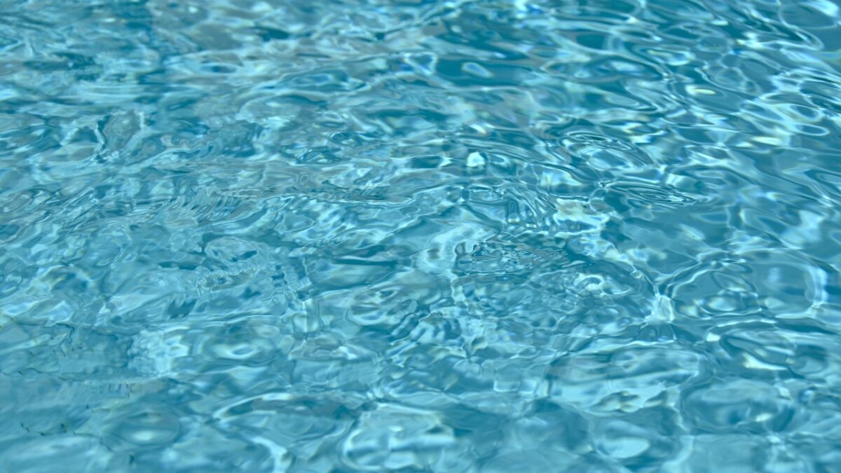 Surface d'eau bleue d'une piscine, avec des ondulations et des reflets lumineux.