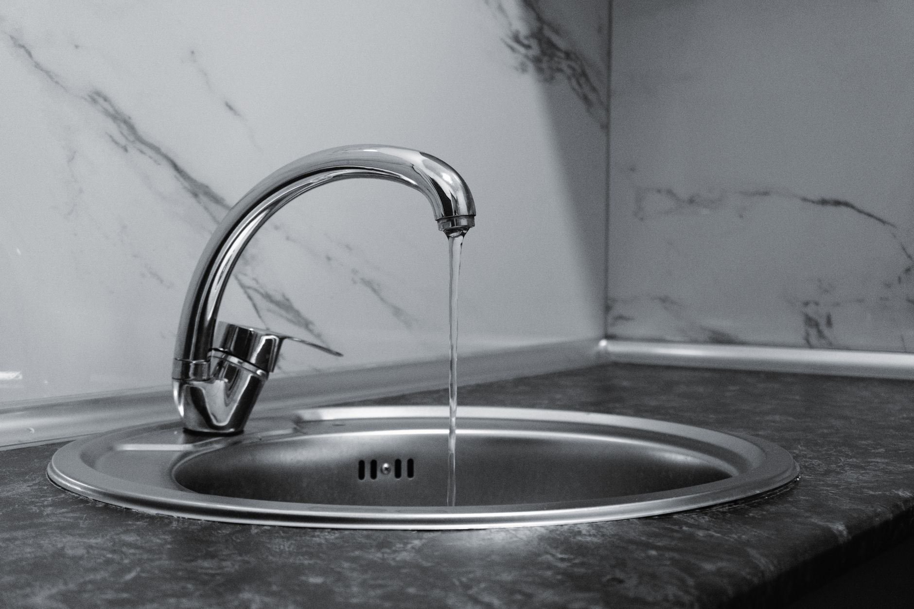 Robinet chromé avec eau courante dans une cuisine moderne avec un comptoir en marbre.