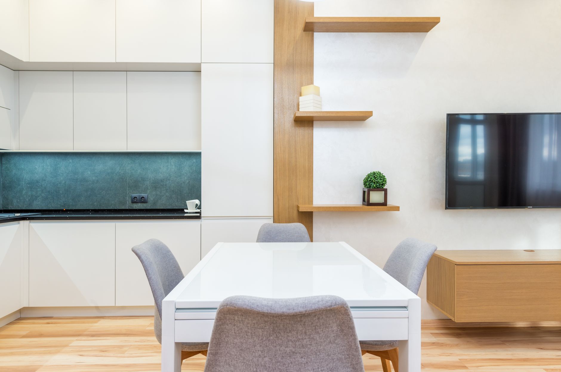 Intérieur d'appartement moderne avec table et chaises à côté d'étagères et cuisine ouverte avec placards près de la télévision murale