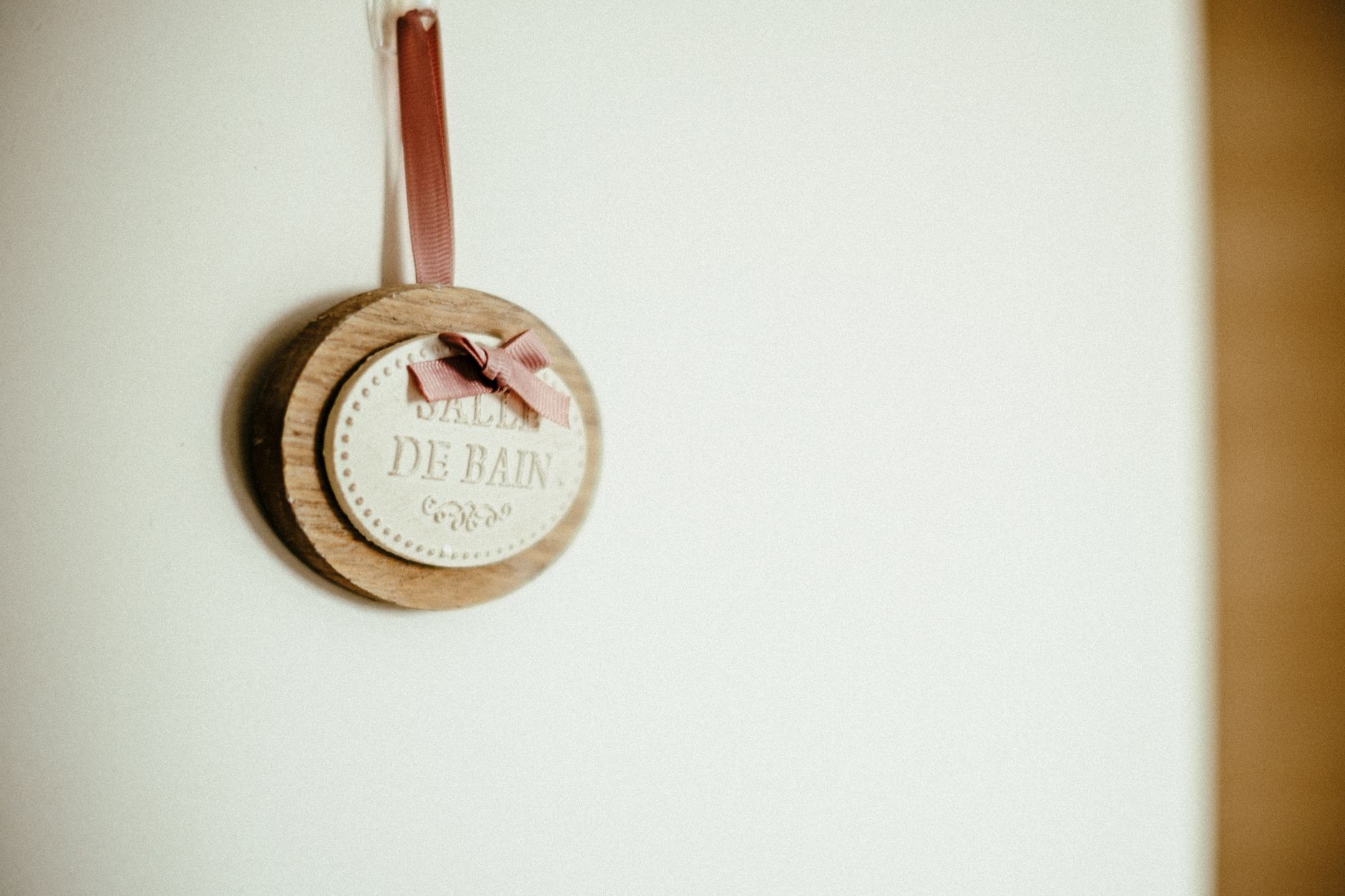 Plaque murale en bois élégante avec le texte 'Salle de Bain', ornée d'un ruban rose, idéale pour la décoration de salle de bain moderne.