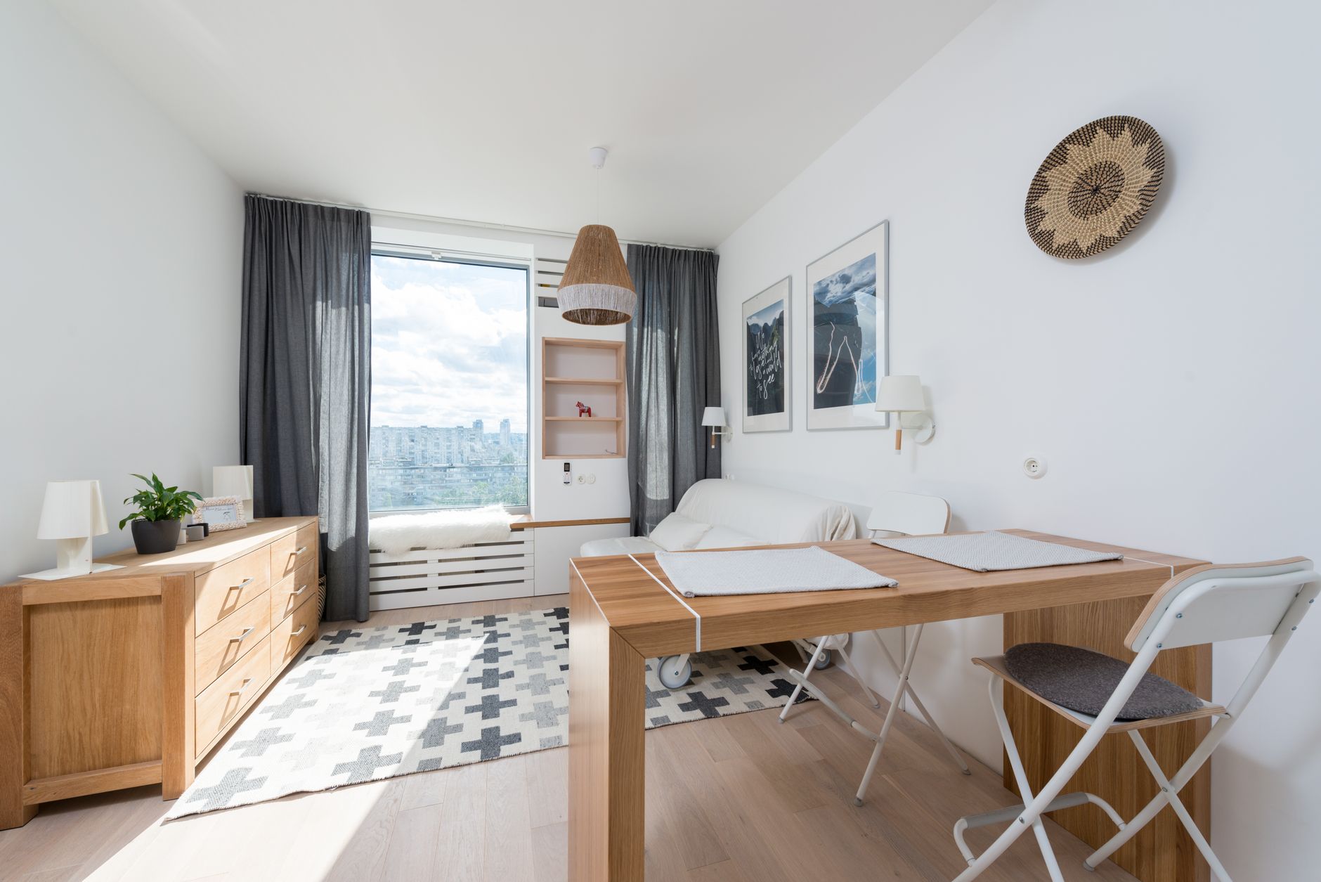 Table avec chaise placée contre une fenêtre avec des rideaux dans une pièce élégante avec un tiroir en bois et un mur décoré de tableaux créatifs