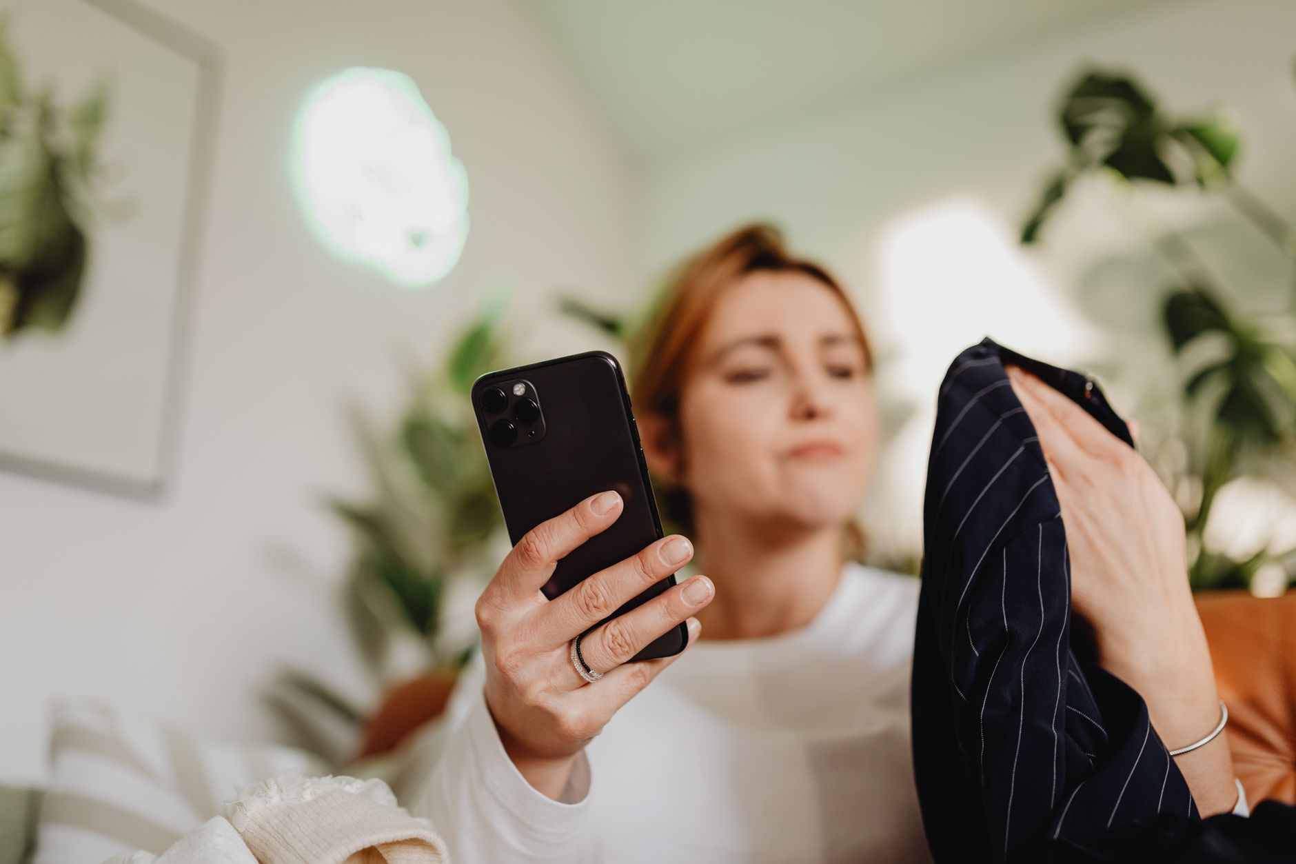 Une femme utilise son smartphone à l'intérieur pour des achats en ligne, tenant du tissu.