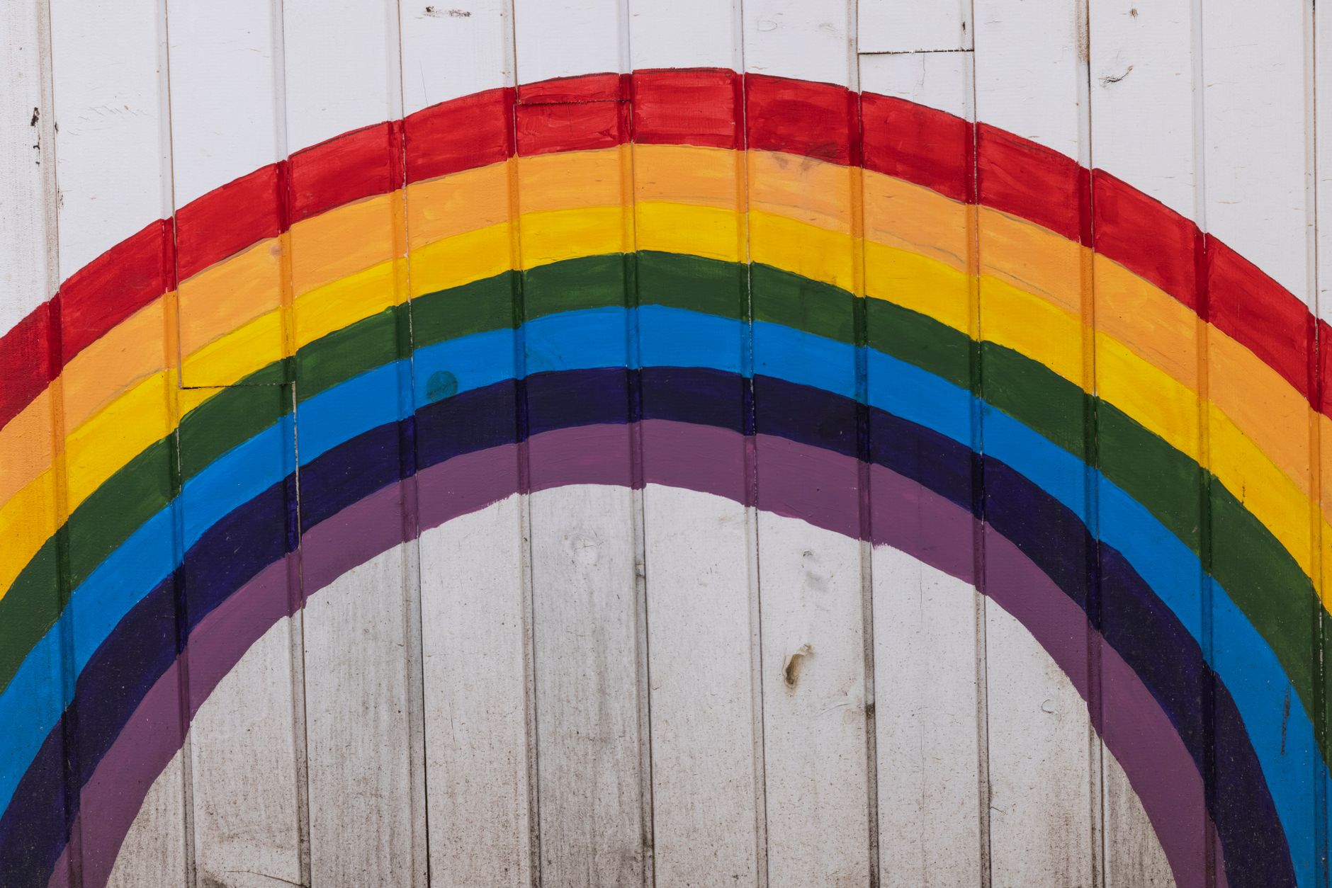 Arc-en-ciel animé peint sur un mur en bois blanc, symbolisant l'espoir et la diversité.
