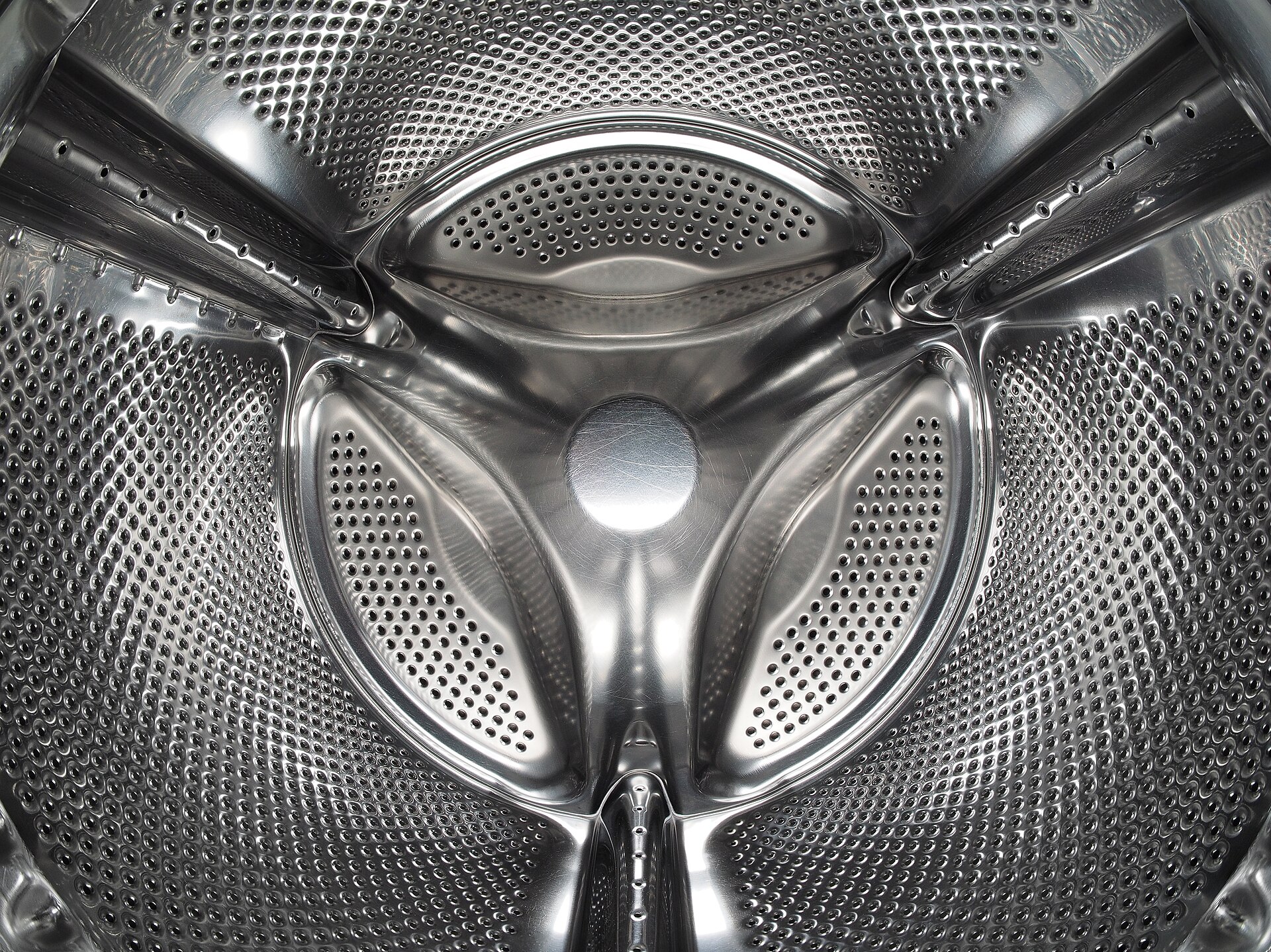Intérieur du tambour inox perforé d’un lave-linge à hublot, avec ses trois aubes