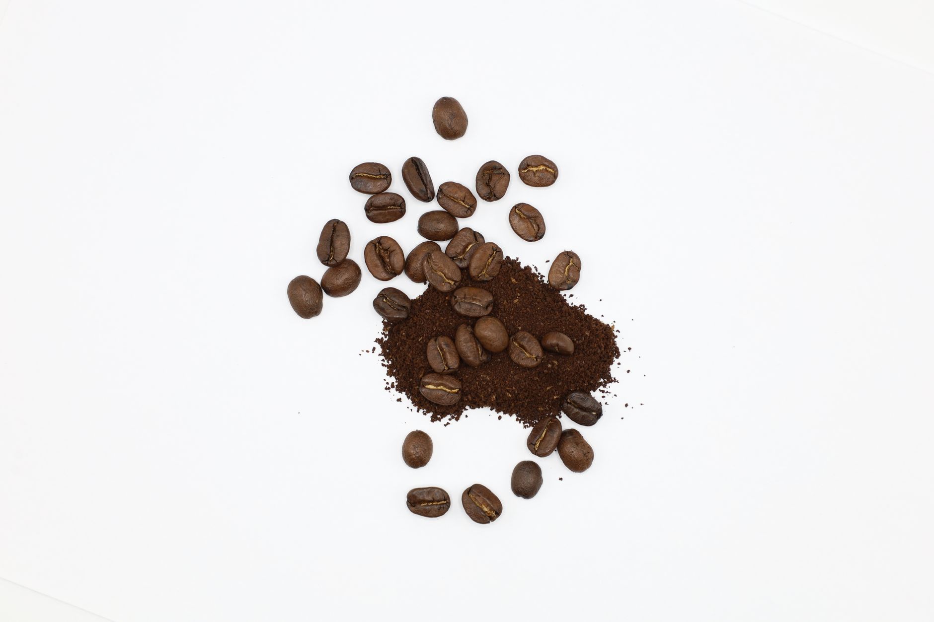 Tas de café moulu et grains de café torréfiés, vus de dessus sur fond blanc uni.